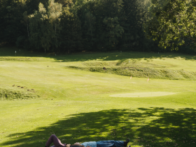 Unter dem sanften Licht der Nachmittagssonne entspannen drei Freunde auf der gr&uuml;nen Wiese, umgeben von der majest&auml;tischen Kulisse der Wiener Alpen. Die ruhige Atmosph&auml;re und das sanfte Rascheln der Bl&auml;tter laden dazu ein, die Seele baumeln zu lassen und die Sch&ouml;nheit der Natur zu genie&szlig;en.