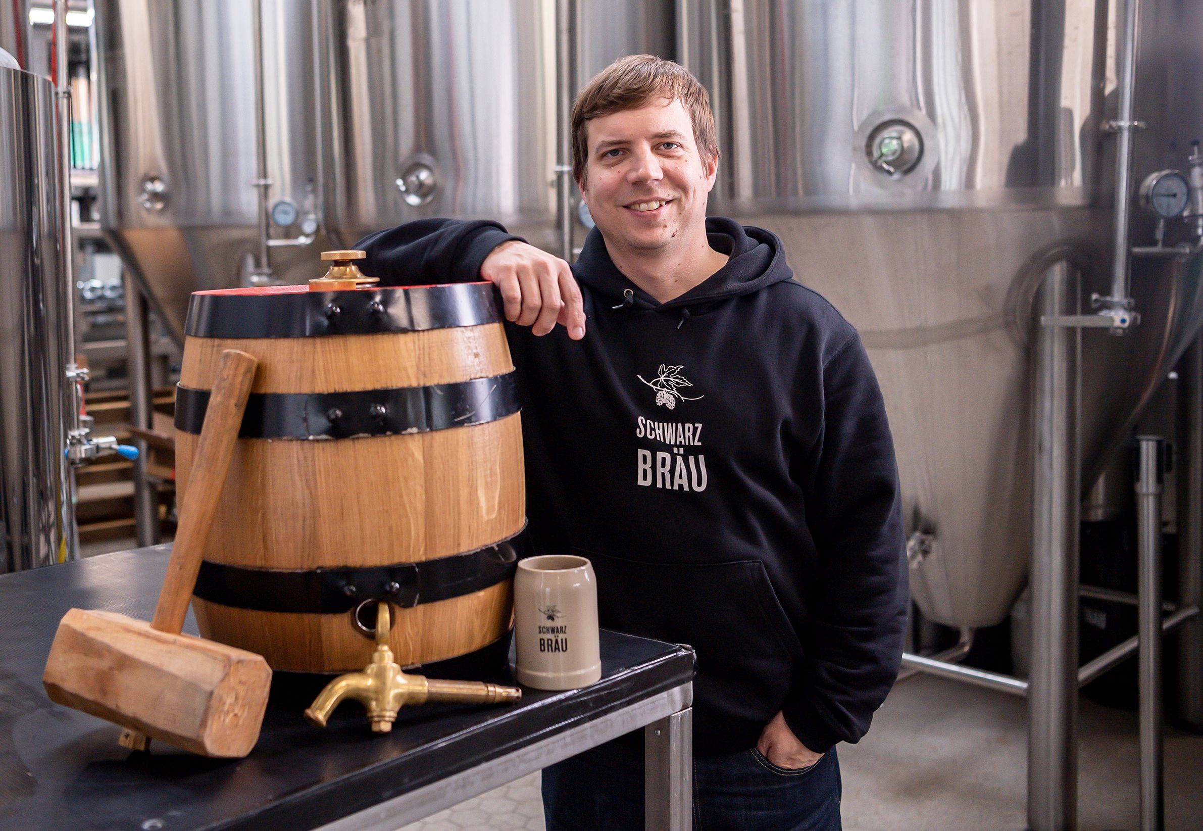 Ein Mann steht in einer Brauerei und lehnt an einem Bierfass.
