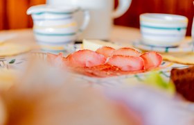 Close-up of a breakfast table with ham, crockery and cups.