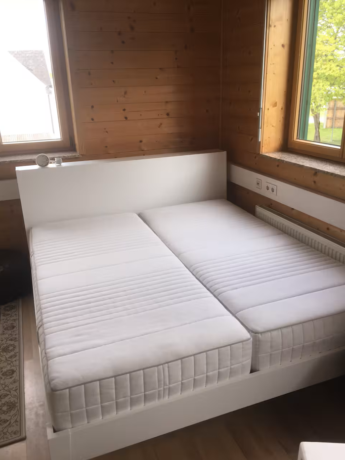 Doppelbett mit 2 Matratzen in einem Zimmer mit Holzvertäfelung und Steckdosen neben dem Bett