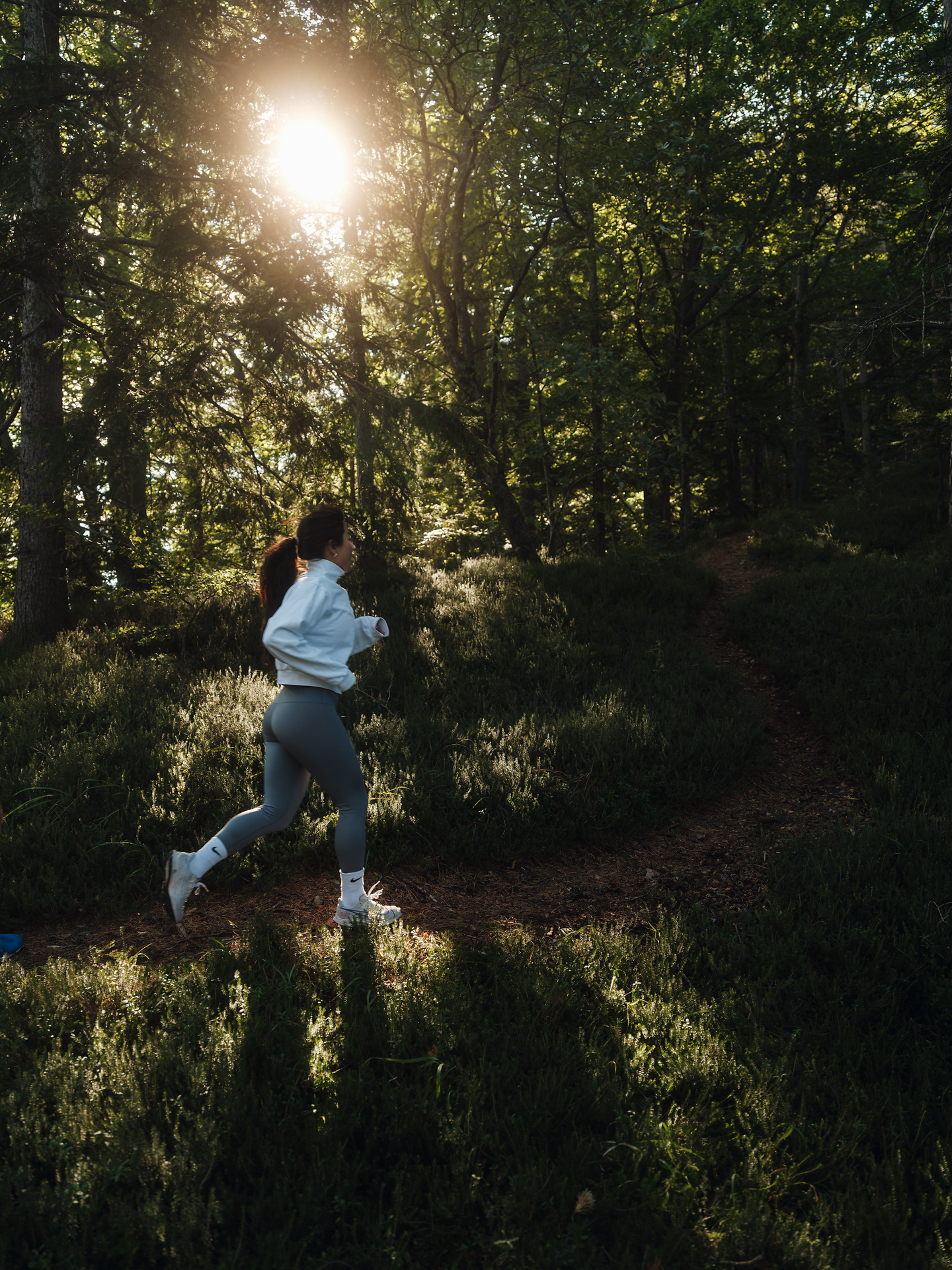 Ein Läufer genießt die frische Luft und die Ruhe der Natur, während die Sonne sanft durch die Bäume strahlt. Der schmale Pfad, umgeben von üppigem Grün, lädt dazu ein, die Schönheit der Umgebung zu erkunden und den Alltag hinter sich zu lassen.