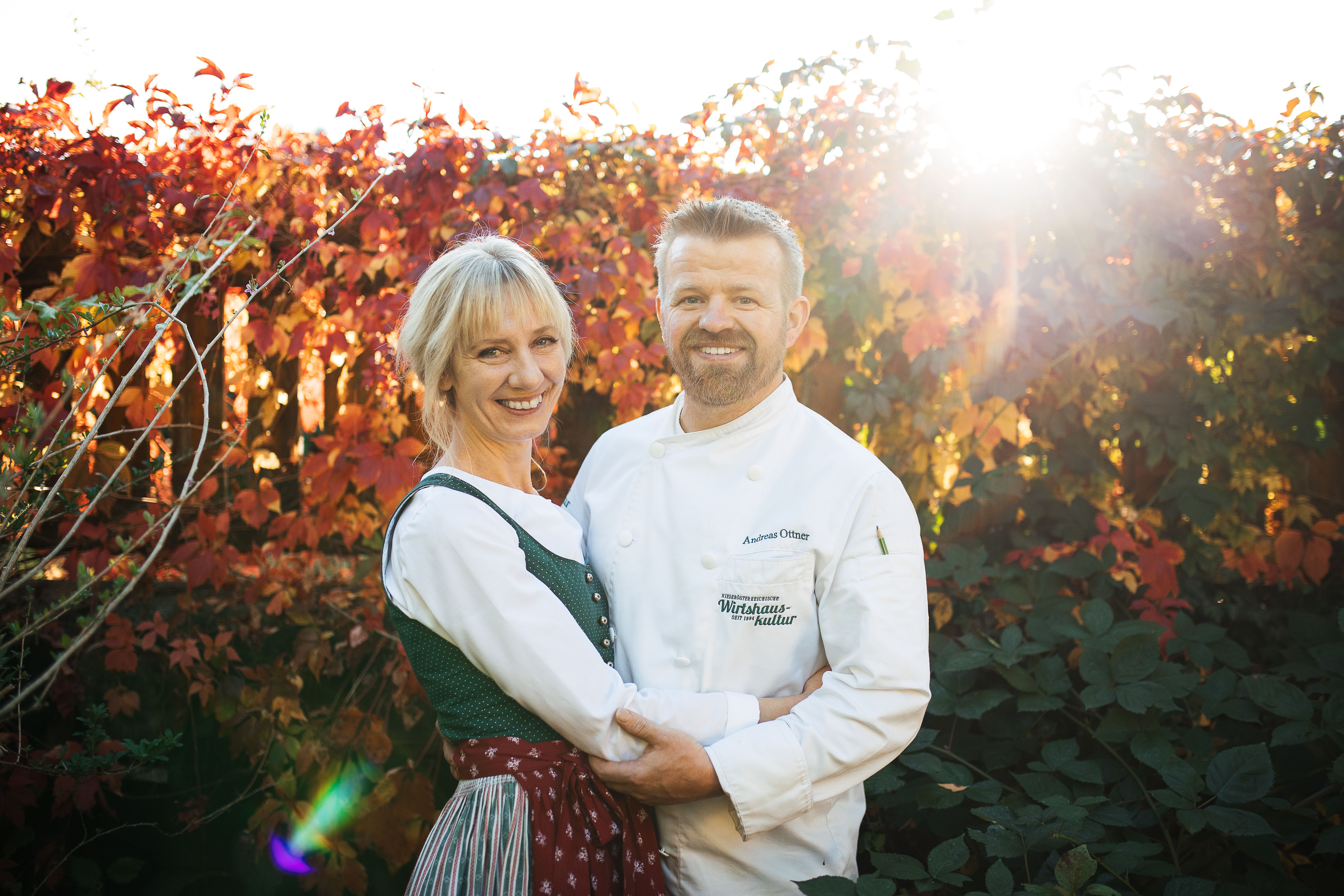 Ein Mann in Kochjacke und eine Frau in traditioneller Kleidung halten sich in den Armen.