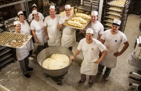 Employees of a bakery in white work clothes with trays full of pasta in a bakery.