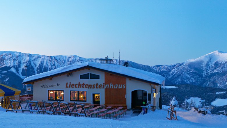 Winterlandschaft mit Liechtensteinhaus und Seilbahn vor schneebedeckten Bergen.