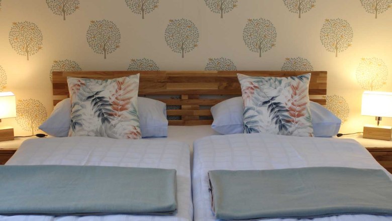 Gem&uuml;tliches Doppelbett mit Holzkopfteil, Decken und Kissen und Nachttischen mit Lampen.