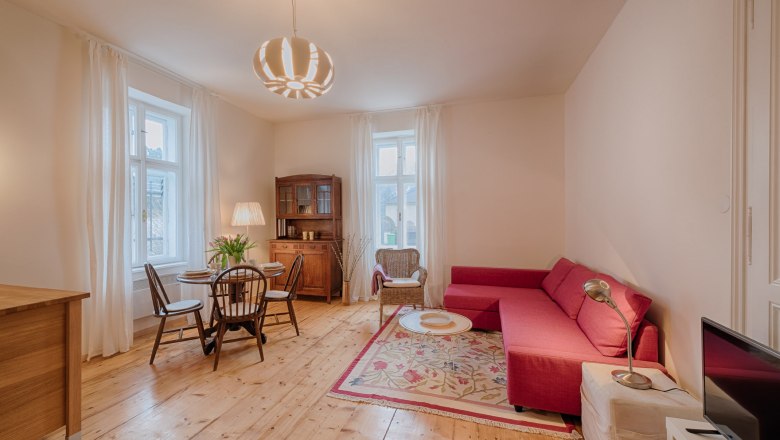 Gemütliches Wohnzimmer mit rotem Sofa, Holzboden und Esstisch.