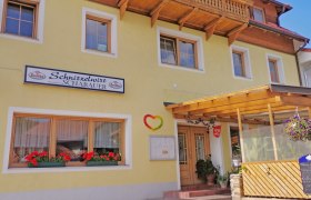 Yellow building with sign 'Schnitzelwirt Schabauer', flower boxes and covered entrance.