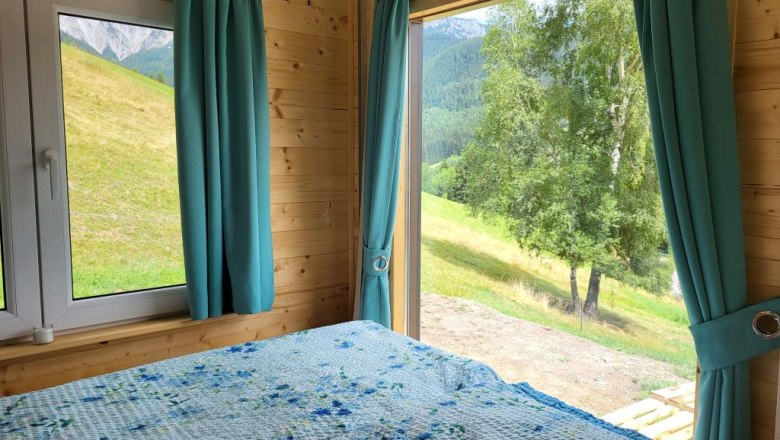 Interior view of a room with a bed and large windows offering a view of a green landscape.
