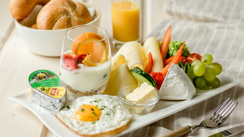 Ein Teller mit vegetarischem Frühstück: Spiegelei, Käse, Gemüse, Joghurt mit Obst, Brötchen und Orangensaft.