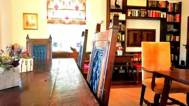 Ein gemütlicher Frühstücksraum mit Holztisch, blauen Stühlen, Bücherregal und dekorativem Fenster.