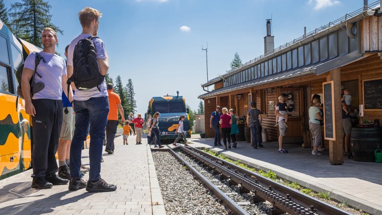People at a station with a train and a wooden building.