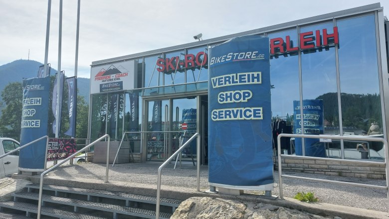 Eingang eines Sportgeschäfts mit Verleih, Shop und Service. Im Hintergrund Berge.