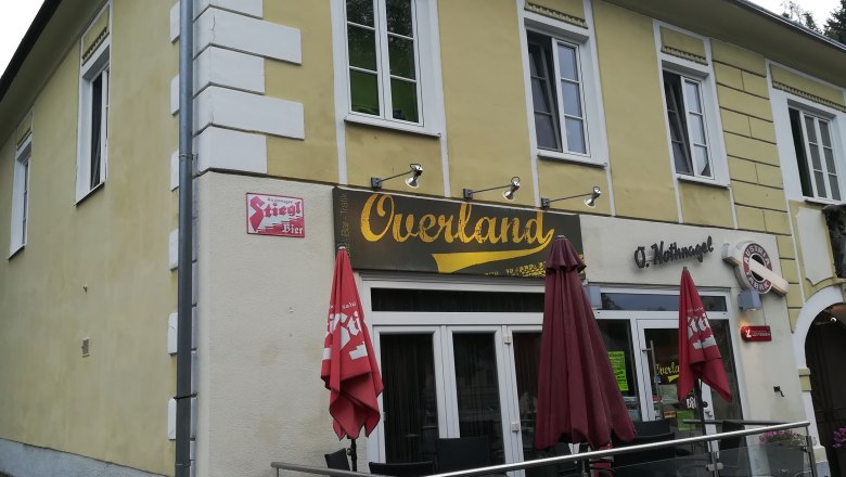 Gelbes Gebäude mit dem Schriftzug 'Overland' und roten Sonnenschirmen.