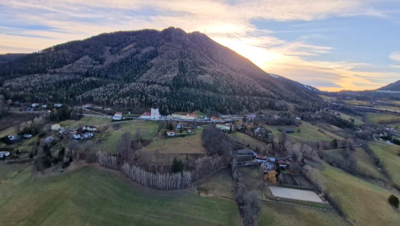 Landschaft mit Kirche und Bergen im Hintergrund bei Sonnenuntergang.