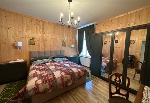 Gemütliches Schlafzimmer mit Holzwänden, Doppelbett, Spiegelkleiderschrank und Kronleuchter.