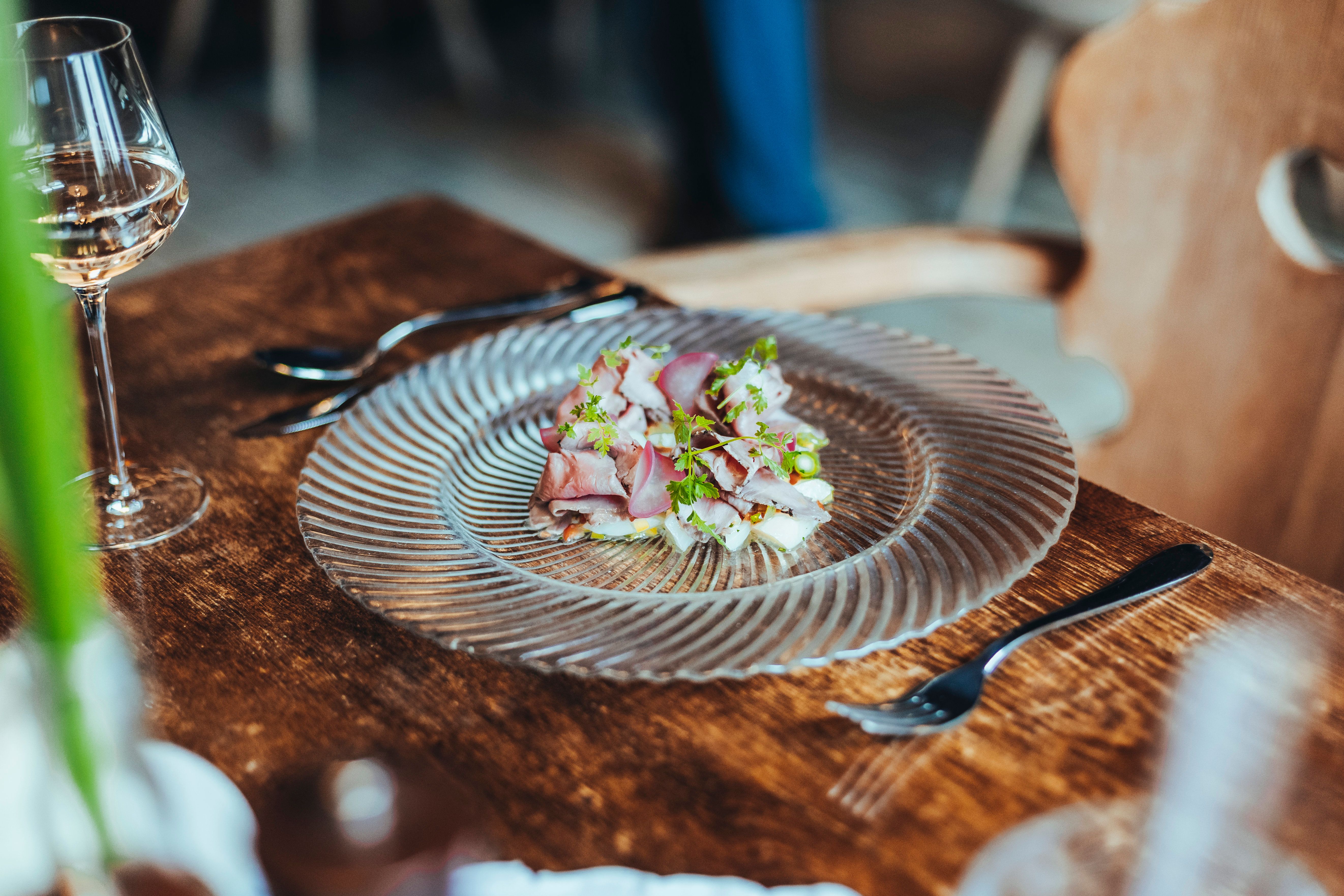 Ein Teller mit Roastbeef und Spargelsalat auf einem Holztisch, daneben ein Glas Weißwein.
