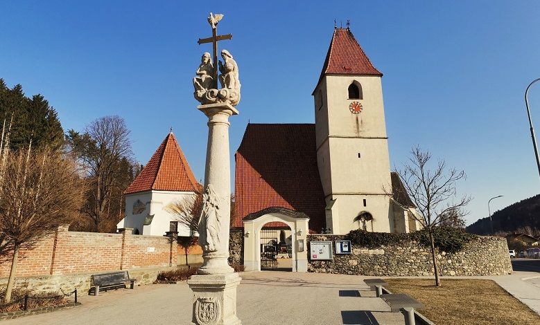 Pfarrkirche Unter-Aspang mit Säule im Vordergrund und blauem Himmel.
