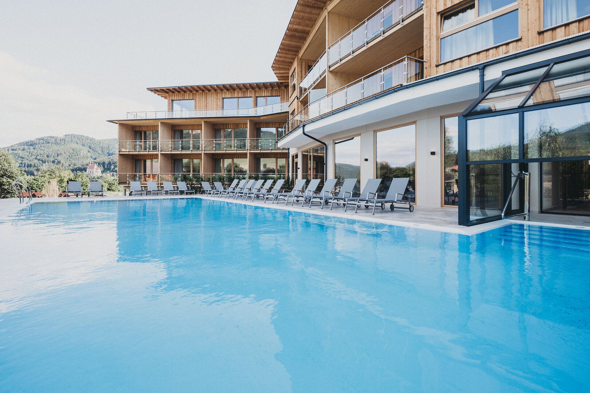 Einladende Sonnenstrahlen tanzen auf der glitzernden Wasseroberfläche des Pools, umgeben von der majestätischen Kulisse der Wiener Alpen. Die stilvollen Liegen laden dazu ein, die Seele baumeln zu lassen und die frische Bergluft zu genießen. Hier wird der Sommer zum unvergesslichen Erlebnis.