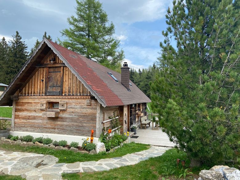 Eine rustikale Holzhütte mit rotem Dach in einer bewaldeten Umgebung, umgeben von Bäumen und einem gepflegten Garten.