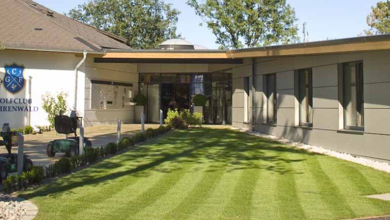 Eingang des Clubhauses des Golfclubs Föhrenwald mit gepflegtem Rasen und modernen Gebäuden.