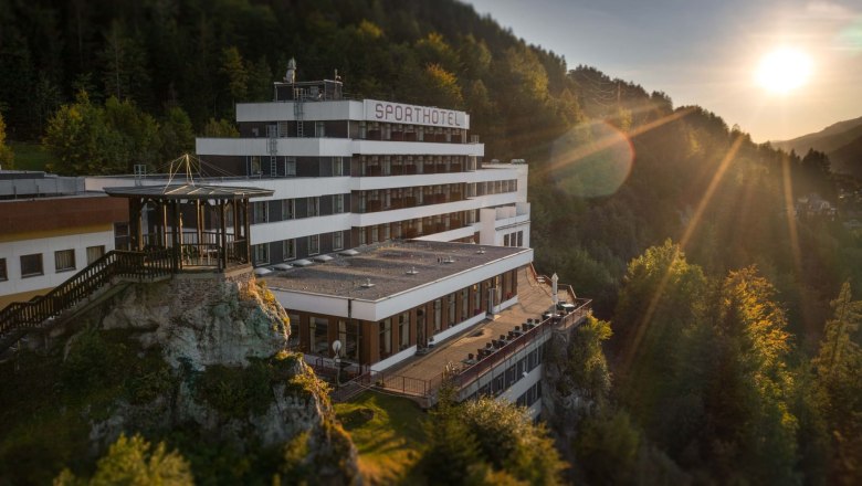 Ein Hotel auf einem Hügel bei Sonnenuntergang, umgeben von Wald.