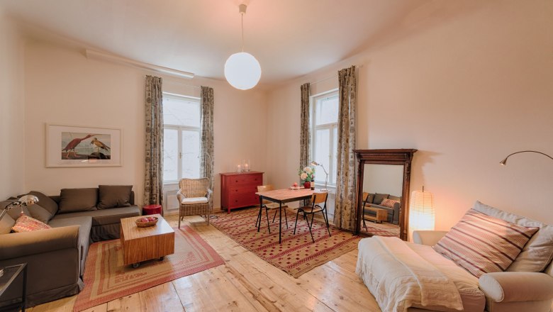 Gemütliches Wohnzimmer mit Holzboden, Sofa, Sessel, Esstisch und großem Spiegel.