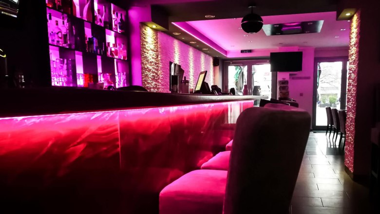 Innenansicht einer stilvollen Bar mit pinker Beleuchtung und moderner Einrichtung.
