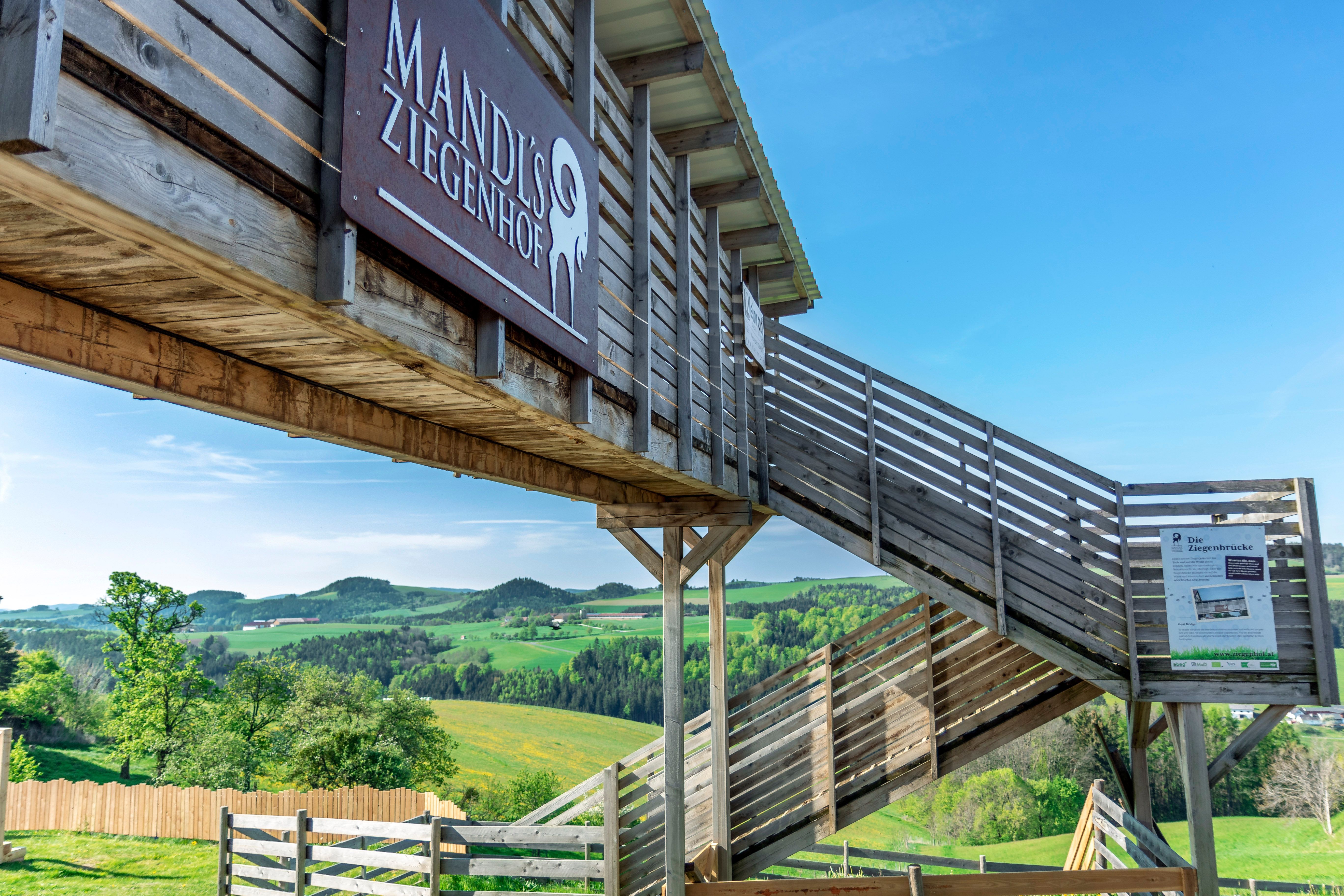 Eine Holzbrücke mit Stiege auf einem Gelände im Freien mit der Aufschrift 'Mandl's Ziegenhof'.