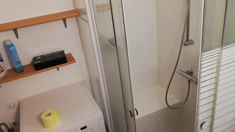 Badezimmer mit Dusche, Waschmaschine und Regalen.