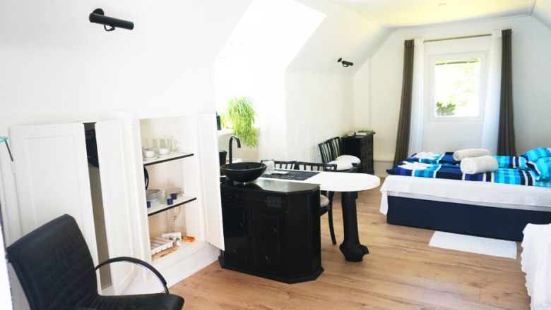 Interior view of a bright vacation home with bed, table, chairs and kitchenette.