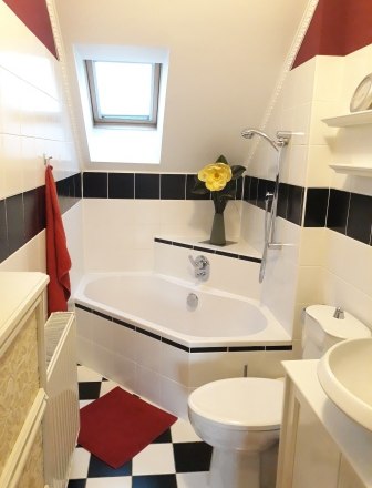 Small bathroom with corner bath, skylight and black and white tiles.