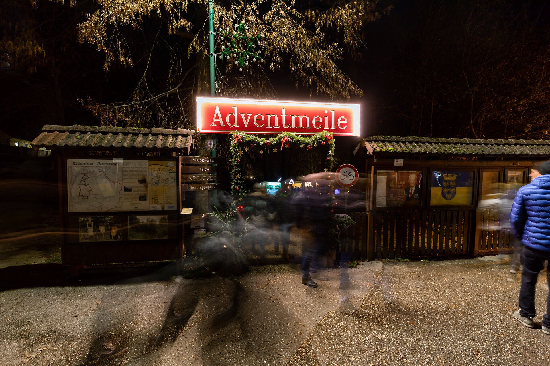 Eingang zu einem Adventsmarkt mit beleuchtetem Schild „Adventmeile“ bei Nacht.