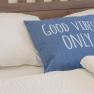 Bett mit blauem Kissen, Aufschrift 'Good Vibes Only'.