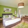 Modern furnished guest room with green accent, double bed, brown armchair and decorative picture on the wall.