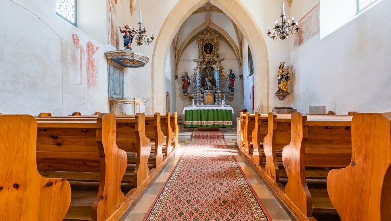 Innenansicht der Wehrkirche Bad Schönau mit Holzbänken, Altar und verzierten Wänden.