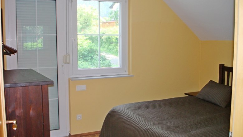 A small bedroom with yellow walls, a single bed and a window with a view of the greenery.