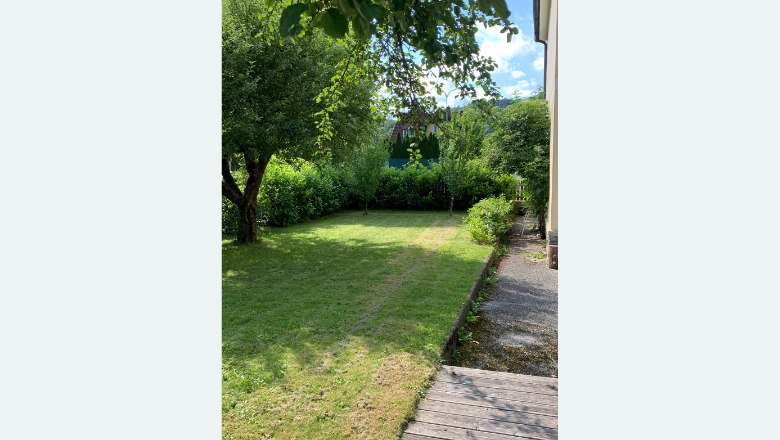 Ein gepflegter Garten mit Rasen, B&auml;umen und Str&auml;uchern neben einem Haus.