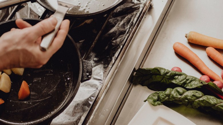 Egy szem&eacute;ly egy darab halat s&uuml;t egy serpenyőben a főzőlapon. Mellette z&ouml;lds&eacute;gek &eacute;s egy t&aacute;ny&eacute;r k&ouml;ret.