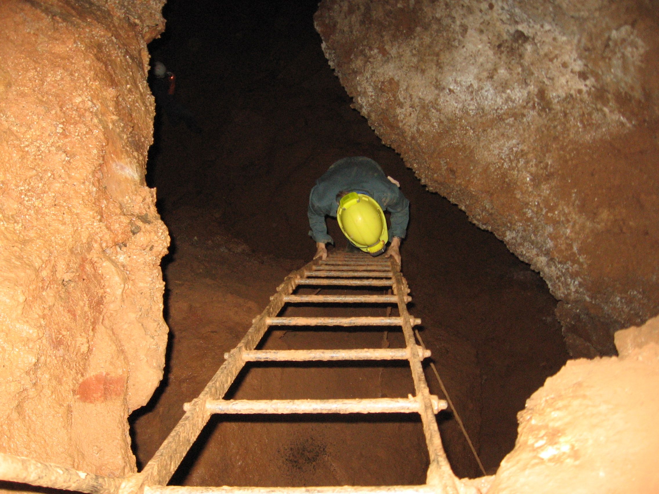 Person mit Helm klettert eine Leiter in einer Höhle hinunter.