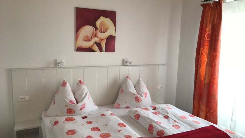 Schlafzimmer mit Doppelbett, Blumenbettwäsche, rotem Bild und Vorhängen.