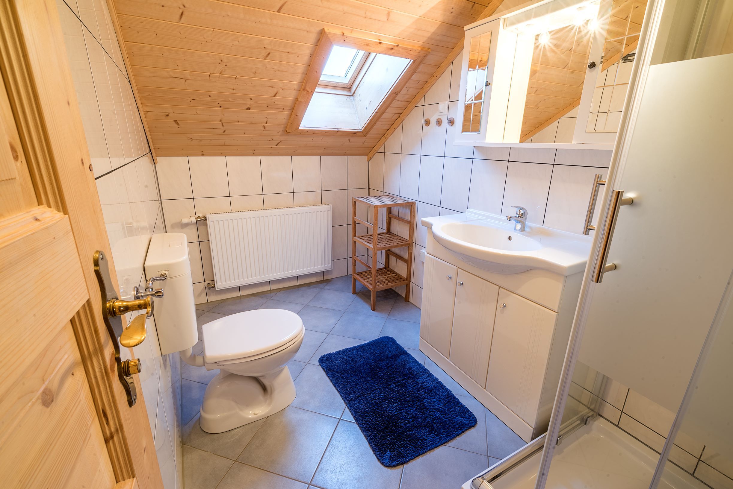 Badezimmer mit Dachschräge, Waschbecken, Toilette, Dusche und blauem Teppich.