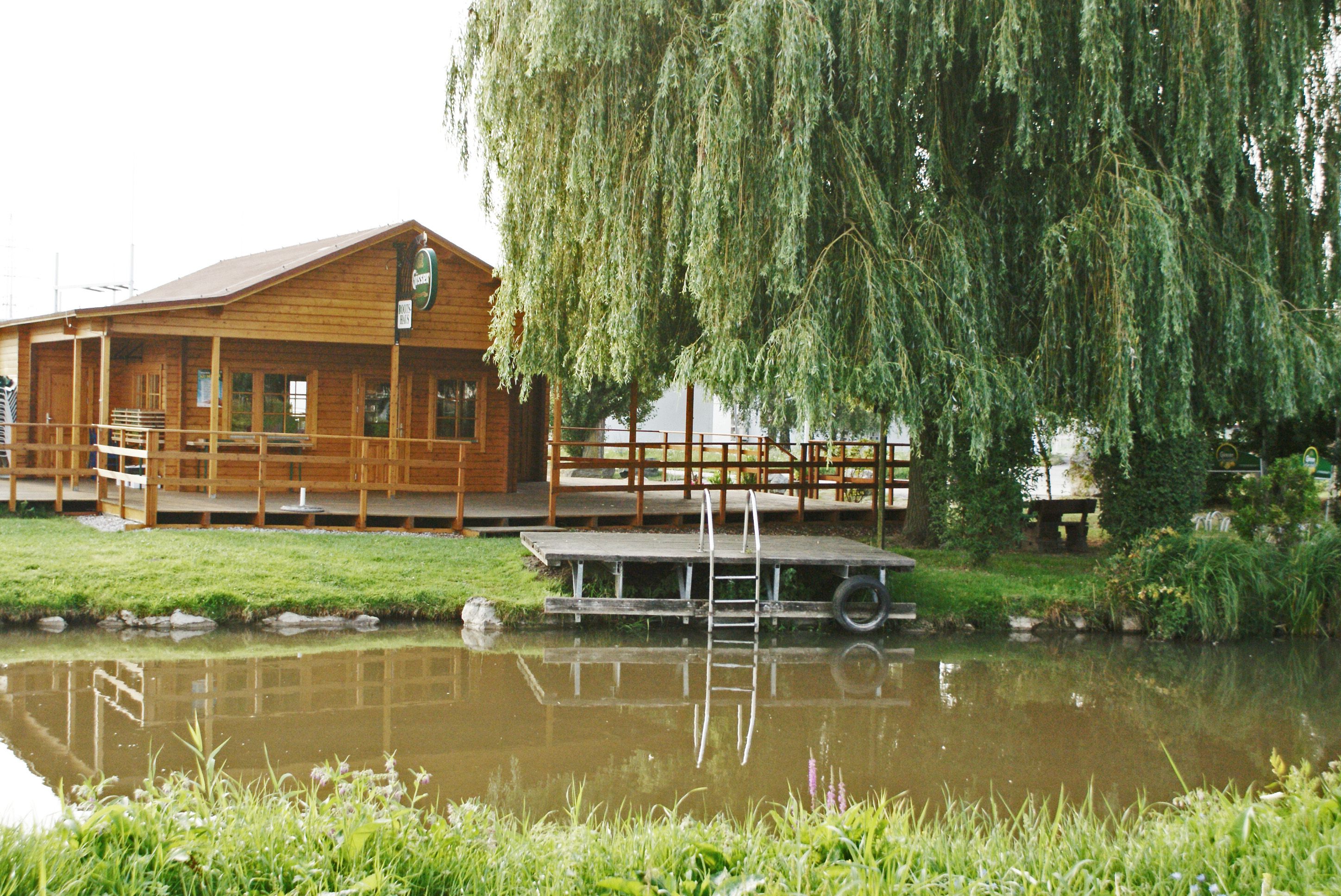 Holzbootshaus am Wiener Neustädter Kanal mit Steg und Weide im Vordergrund.