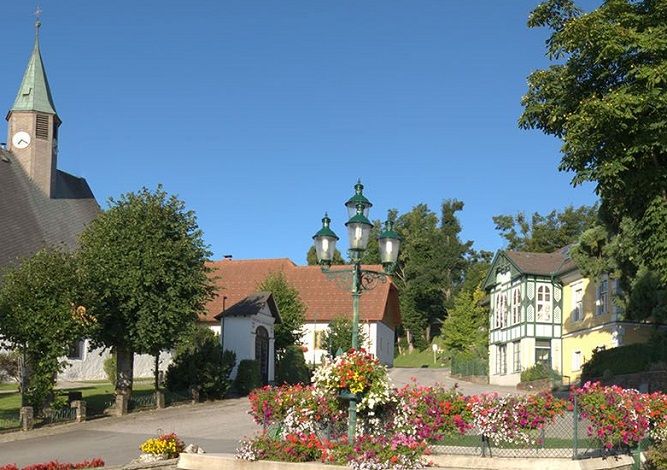 Hauptplatz in Mönichkirchen mit Kirche, Blumen und historischen Gebäuden.