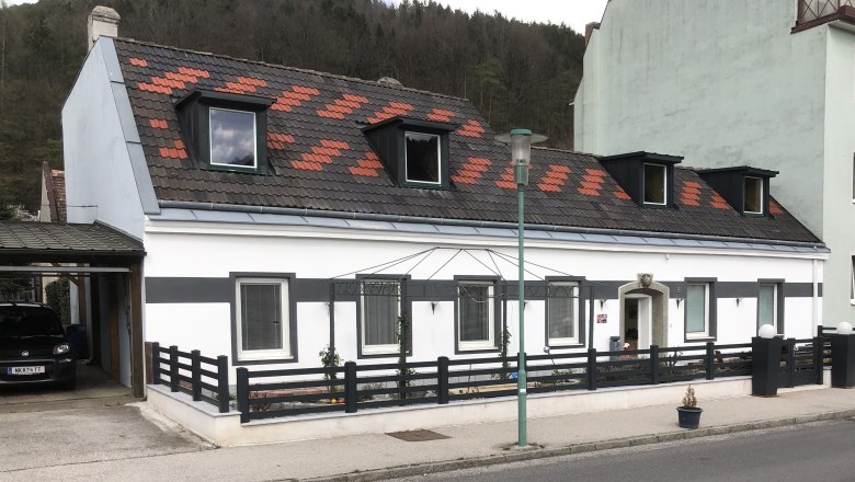 Ansicht eines weißen Hauses mit schwarzem Zaun und Dachfenstern.