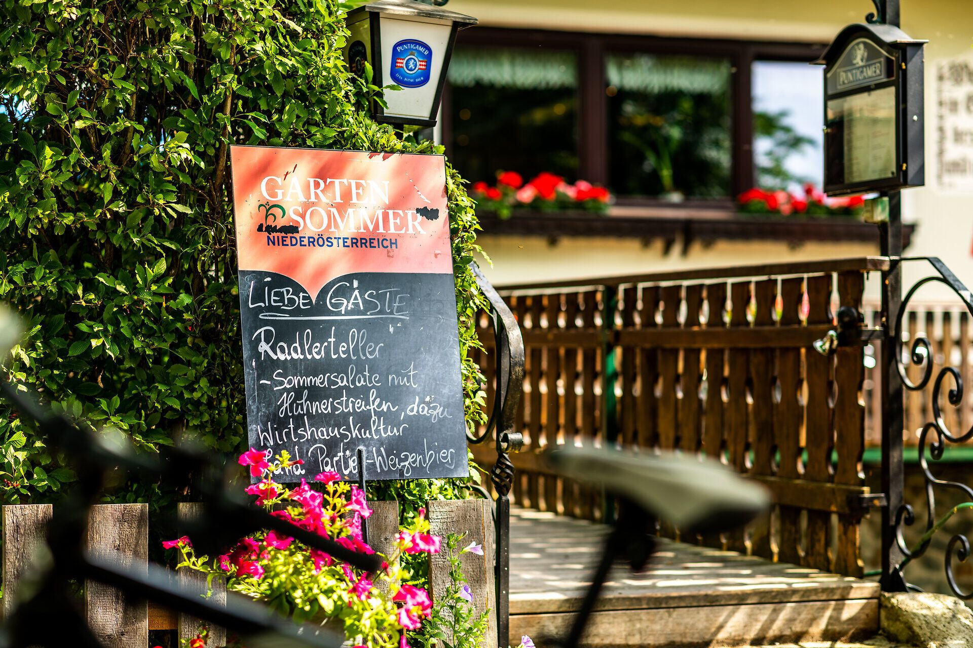 Eine Menütafel am Weg zum Eingang in den Gasthof Pension St. Wolfgang empfiehlt den Gästen einen "Radlerteller" sowie ein Weizenbier.