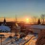 Winter sunrise over a snowy landscape with a church and houses.