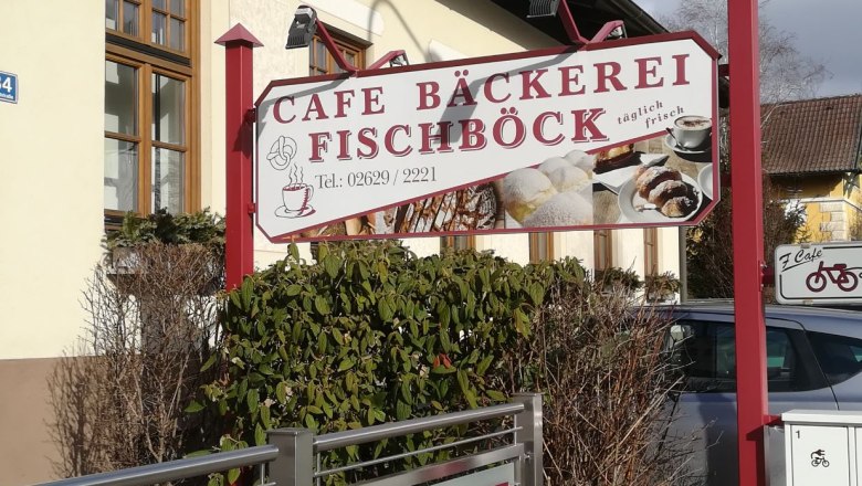 Schild der Caf&eacute;-B&auml;ckerei Fischb&ouml;ck mit Geb&auml;ckabbildungen und Telefonnummer.