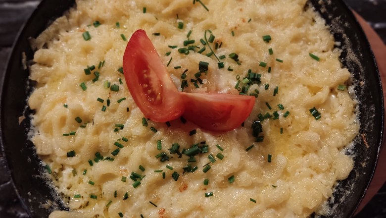 Eine Pfanne mit Käsespätzle, garniert mit Tomaten und Schnittlauch.