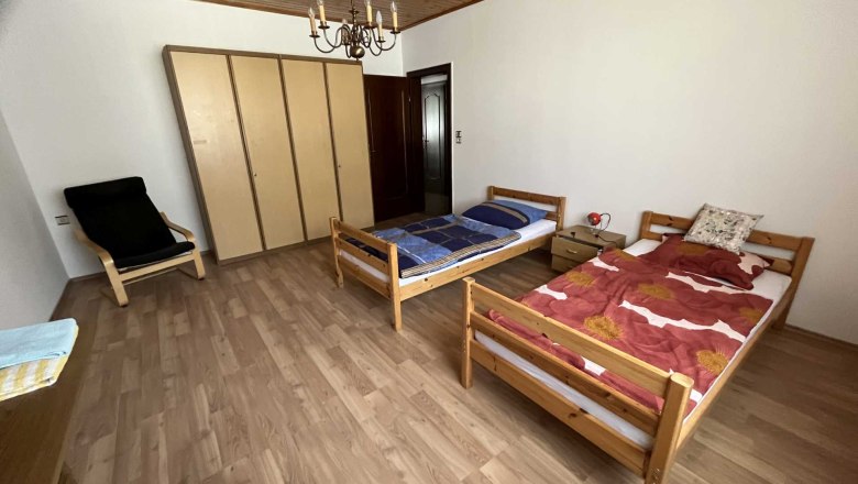 A simply furnished bedroom with two single beds, a closet and an armchair.