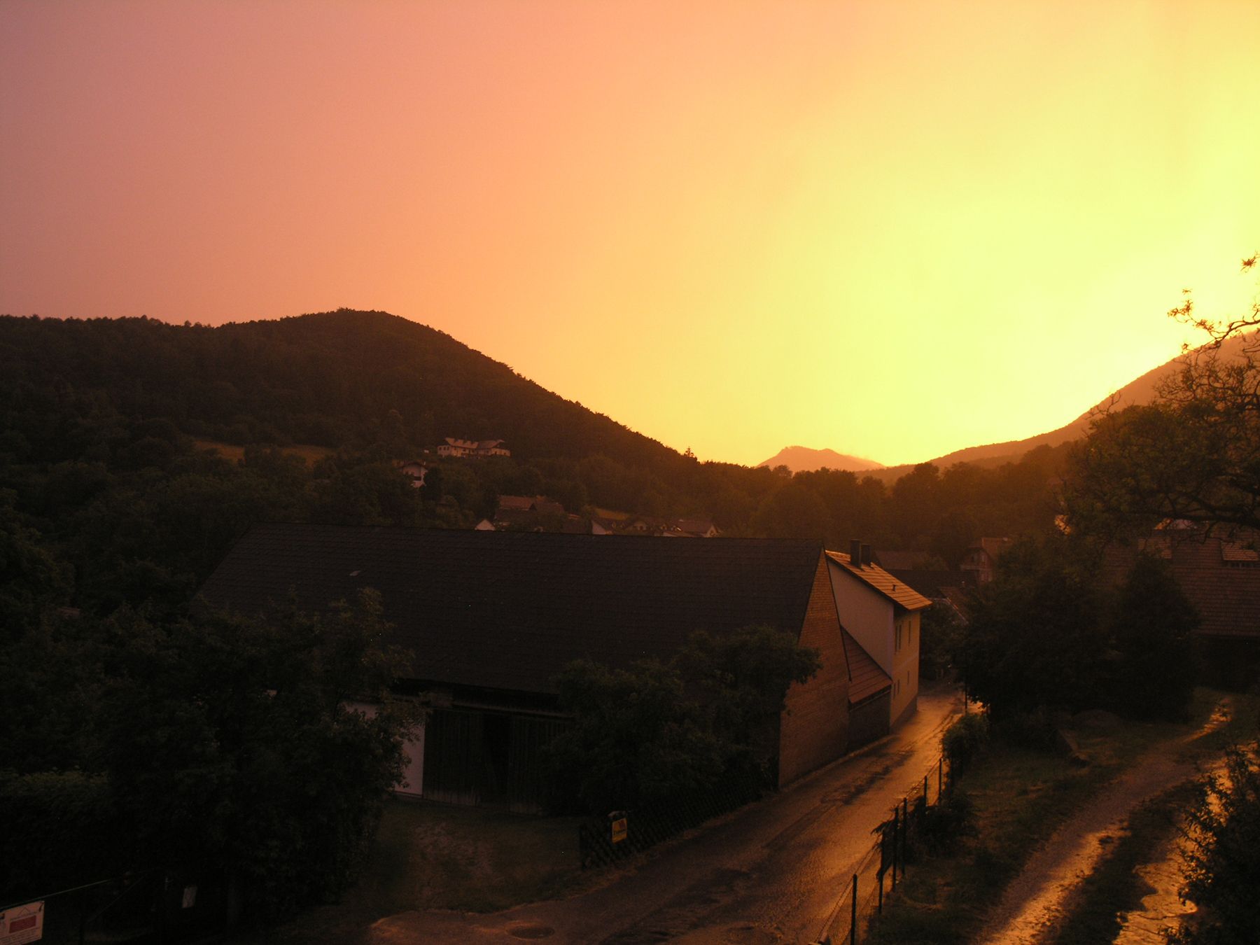 Dorfstraße bei Sonnenuntergang mit Hügeln im Hintergrund.